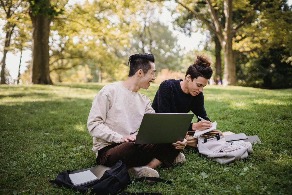 Two men sitting in a park, brainstorming and writing. This image introduces the blog post titled "What Is a Tagline? 50+ Brilliant Tagline Examples"