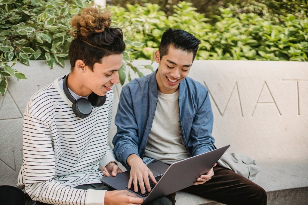 Zwei Männer arbeiten draußen an einem Laptop und sehen glücklich aus. Dies ist das Intro zu einem Artikel über Employer Branding, auch bekannt als Arbeitgeber-Branding.