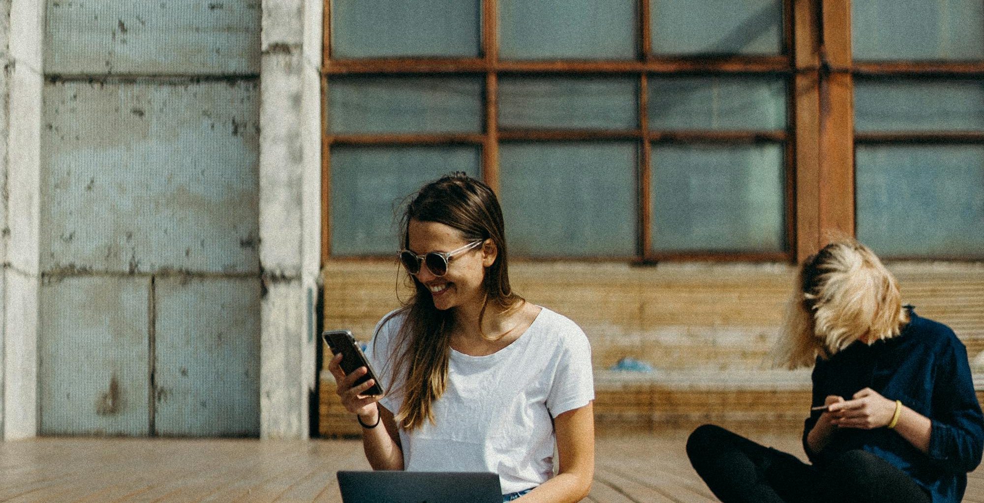 Two woman sitting outside, working on their phones as an introduction to my article "20 Proven Ways to Build Brand Awareness Organically"