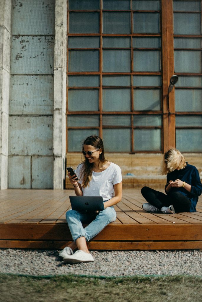 Two woman sitting outside, working on their phones as an introduction to my article "20 Proven Ways to Build Brand Awareness Organically"