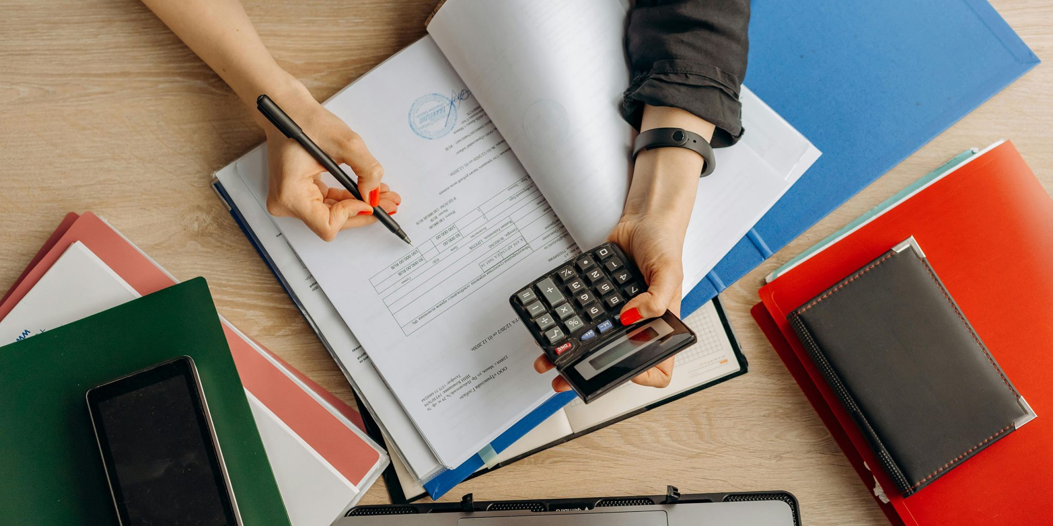 A close-up of hands reviewing documents at a desk, with folders and a calculator visible—setting the scene for an article about conducting a brand audit as a small business.